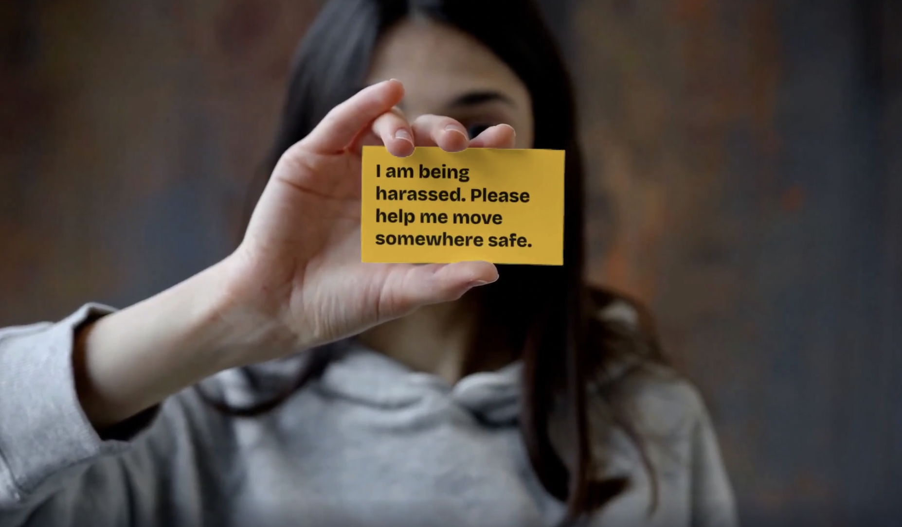A person with long dark hair holds up a yellow script card in front of their face